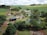 An aerial view of a rural landscape featuring a farmhouse surrounded by lush greenery and multiple small ponds. The property includes solar panels on the building roofs, and is set amidst rolling fields and scattered trees. The sky is overcast with clouds, adding depth to the scenery.