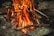 A campfire with vivid flames rises among neatly arranged rocks. The firewood is comprised of sticks and branches, generating a warm, glowing light.