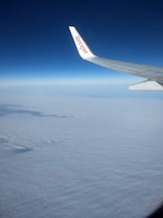 A clear view from an airplane window showing the wingtip of an aircraft with the SpiceJet logo against a backdrop of a vast cloudscape and deep blue sky.