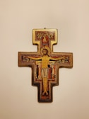 A detailed religious icon depicting the crucifixion with central figure of a man in a loincloth surrounded by smaller figures in traditional robes. Gold, red, and dark colors dominate the intricate design with symbolic Christian elements.