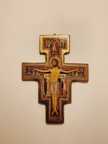 A detailed religious icon depicting the crucifixion with central figure of a man in a loincloth surrounded by smaller figures in traditional robes. Gold, red, and dark colors dominate the intricate design with symbolic Christian elements.