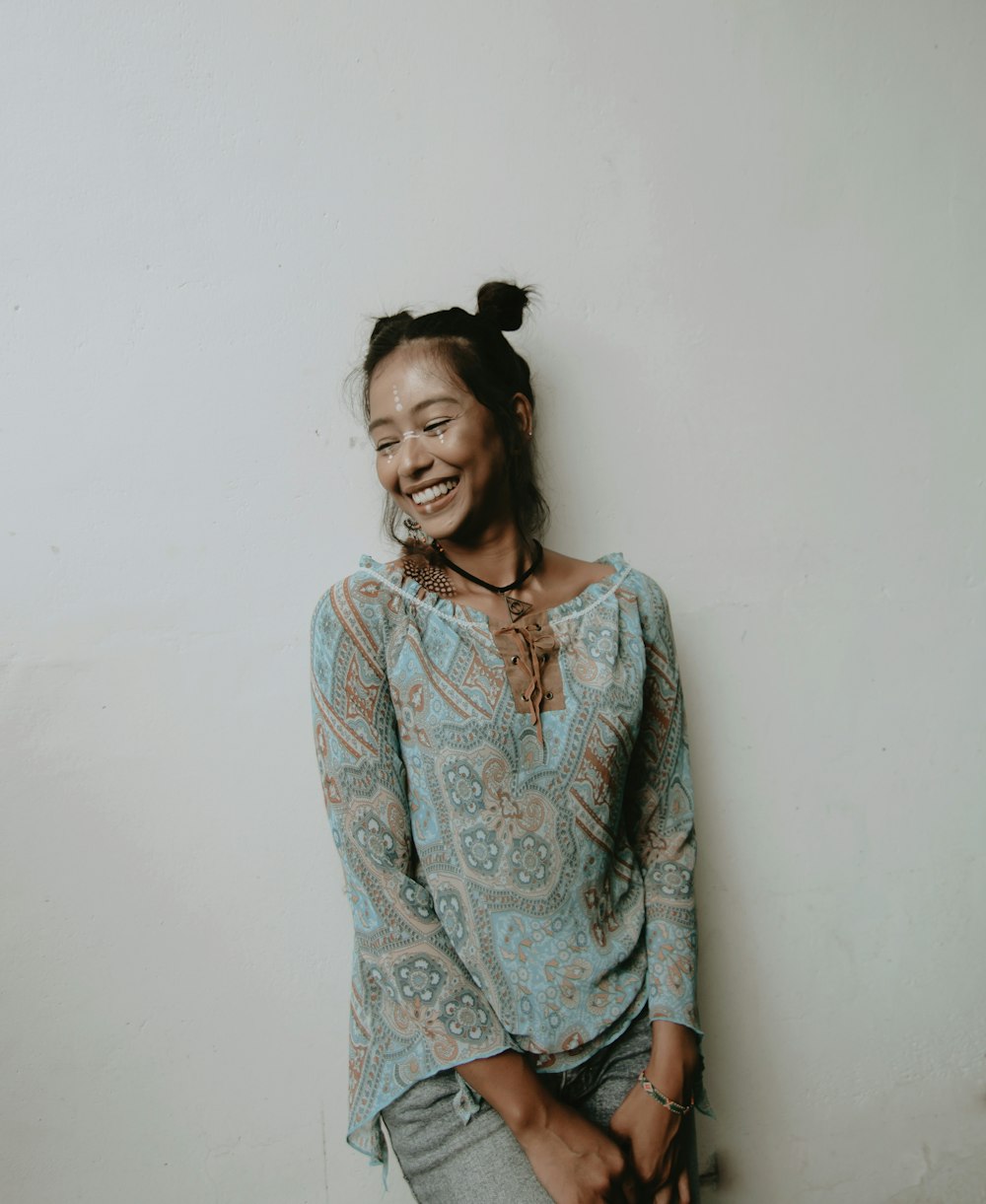 smiling woman wearing blue blouse leaning on wall