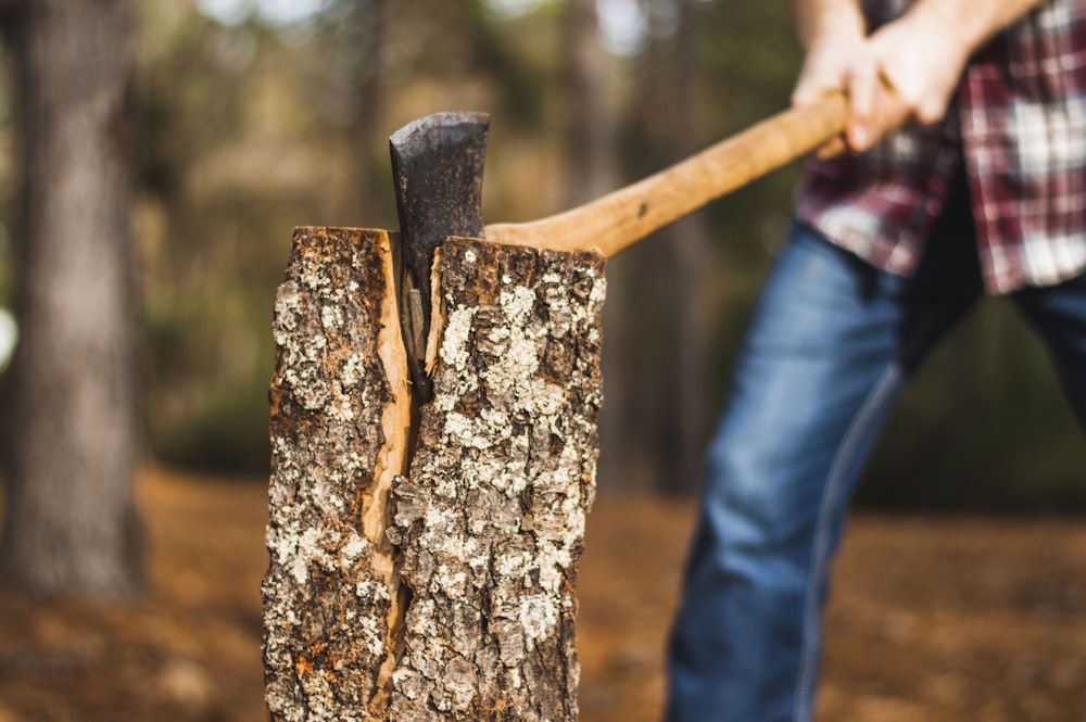 man holding brown axe towards firewood on selective focus photography