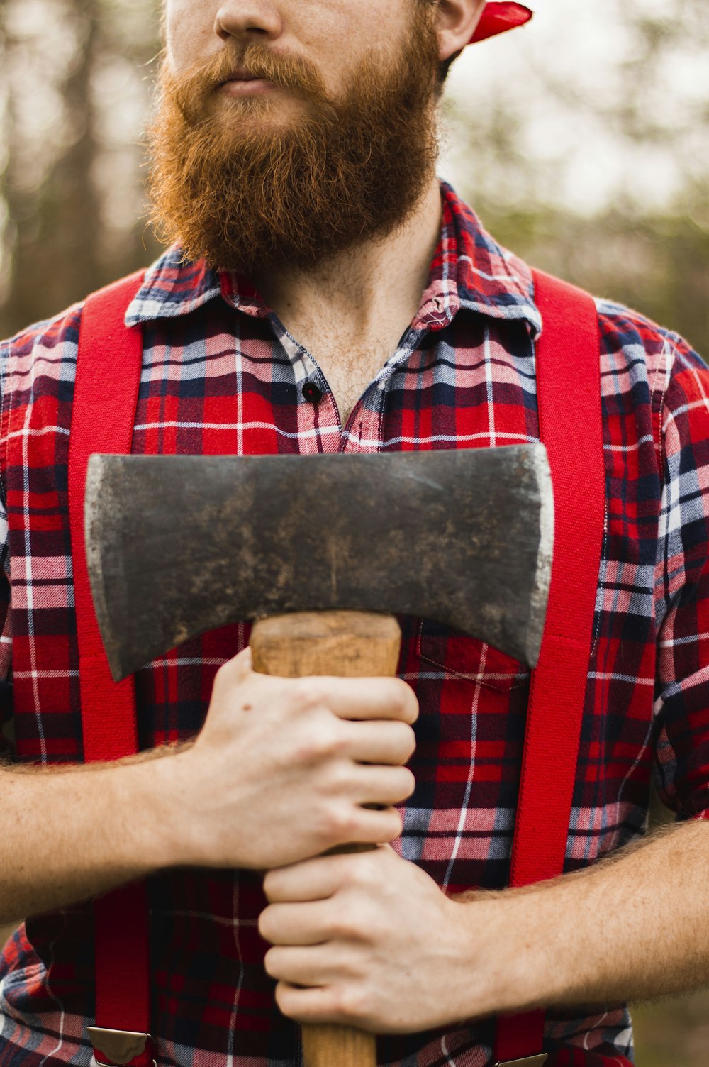 man holding red, blue, and white plaid shirt holding ax