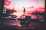 A close-up view of a computer keyboard with a fitness tracker resting on top, set against a blurred background displaying a sunset over a cityscape on a monitor.