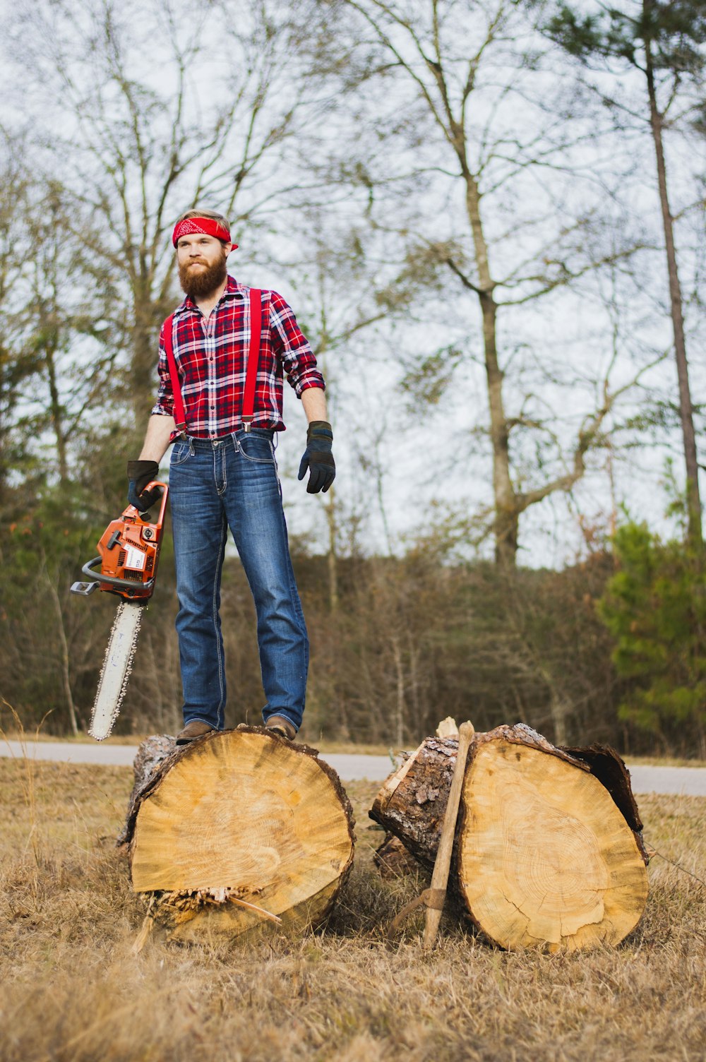 hombre sosteniendo una motosierra y parado sobre un tronco de madera