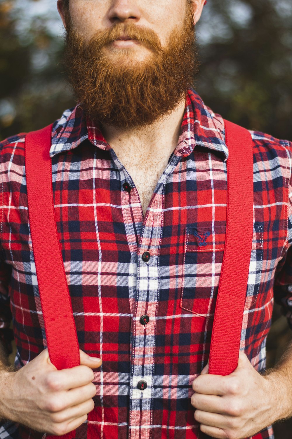 homme en chemise à carreaux rouge, bleu et blanc avec bretelle rouge pendant la journée