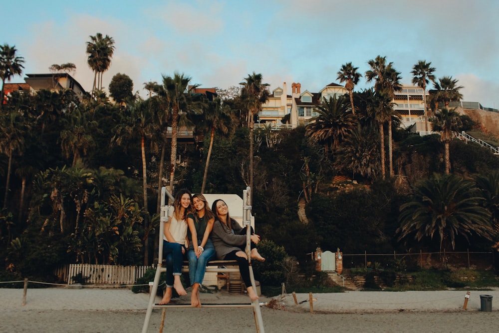 three woman sitting on bench near trees under gray sky