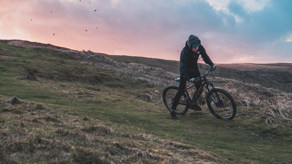 man riding bicycle on grass field under gray sky