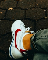 Close-up of trendy sneakers paired with rolled-up jeans on a cobblestone street.