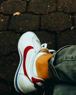 Close-up of trendy sneakers paired with rolled-up jeans on a cobblestone street.