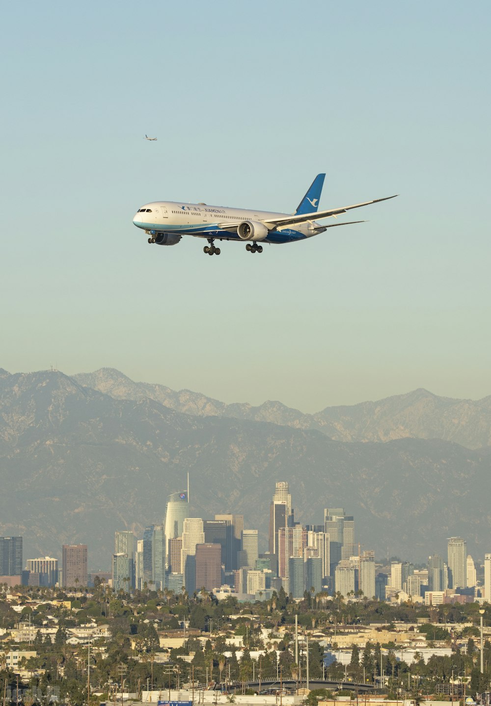 Avión de pasajeros blanco y azul en vuelo sobre edificios