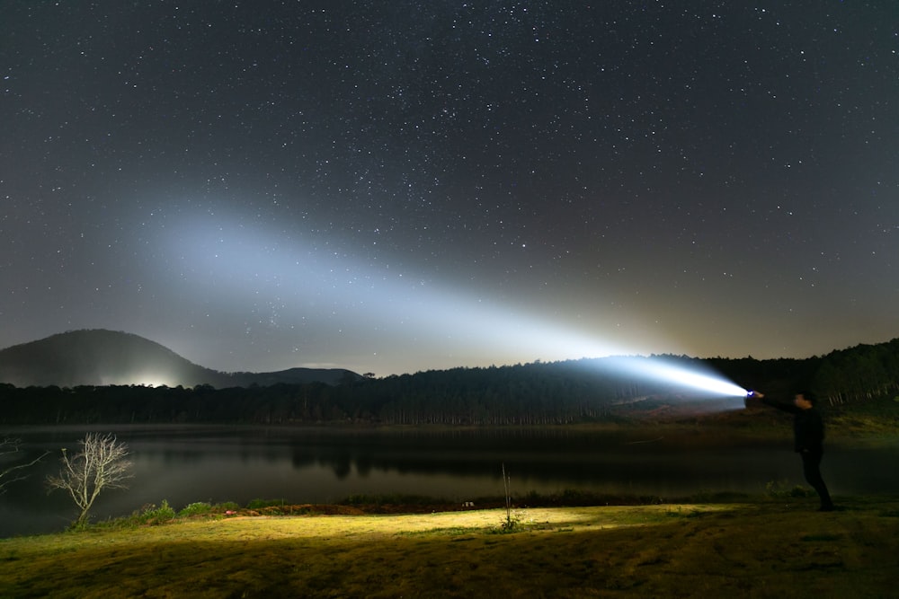 a person holding a flashlight in front of a lake