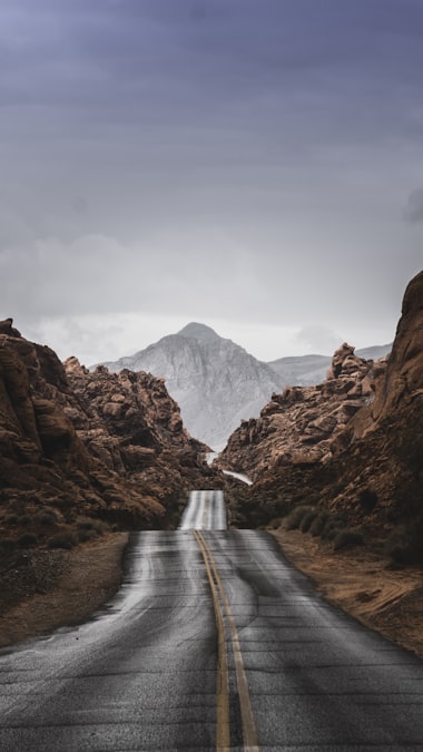 An empty paved road heading through red rock canyon walls toward a distant mountain