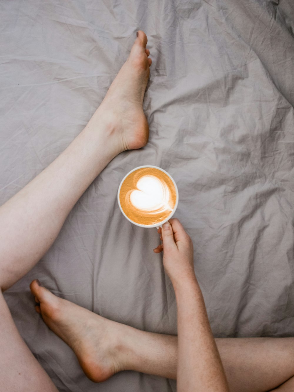 person holding white mug sitting on bed