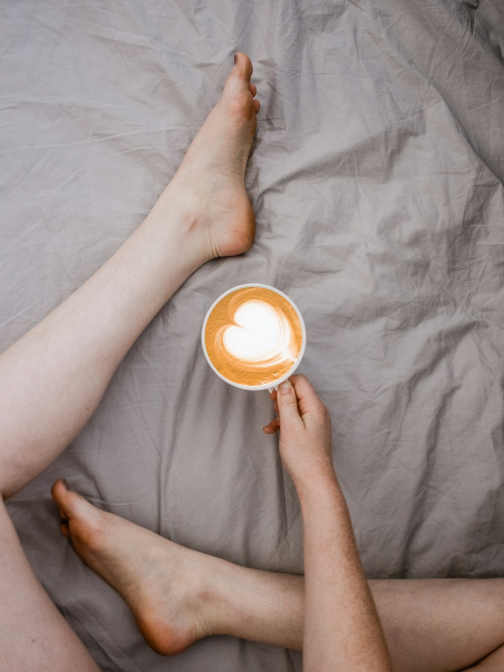 Persona sosteniendo una taza blanca sentada en la cama