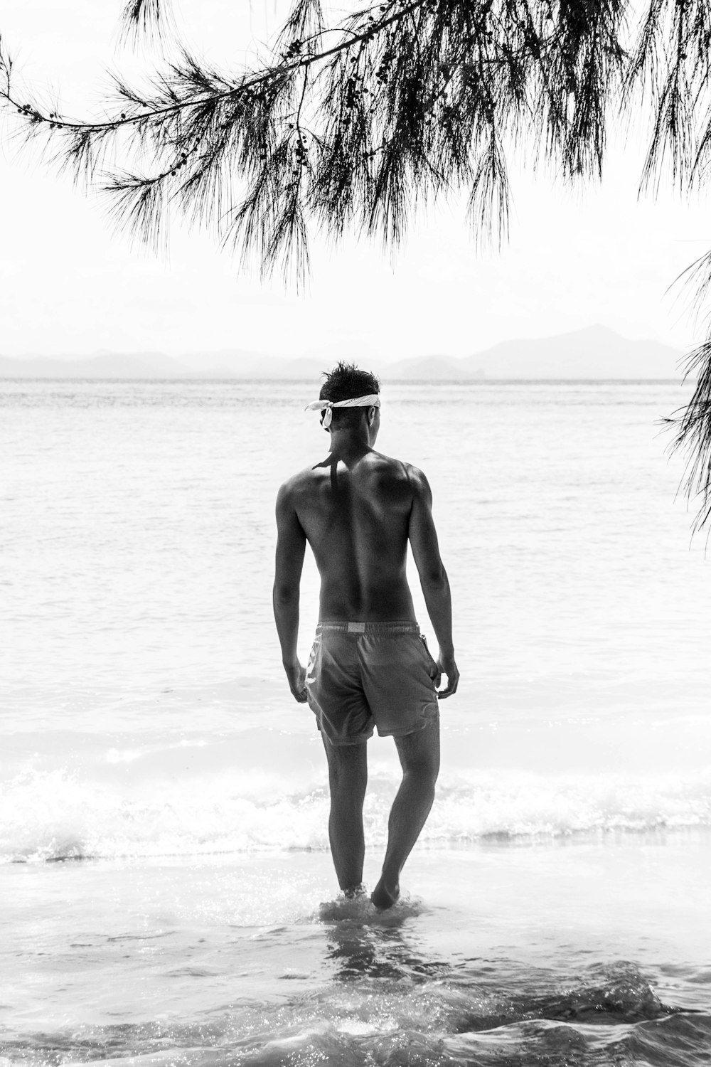 half naked man in shorts with white bandana standing on shore during daytime