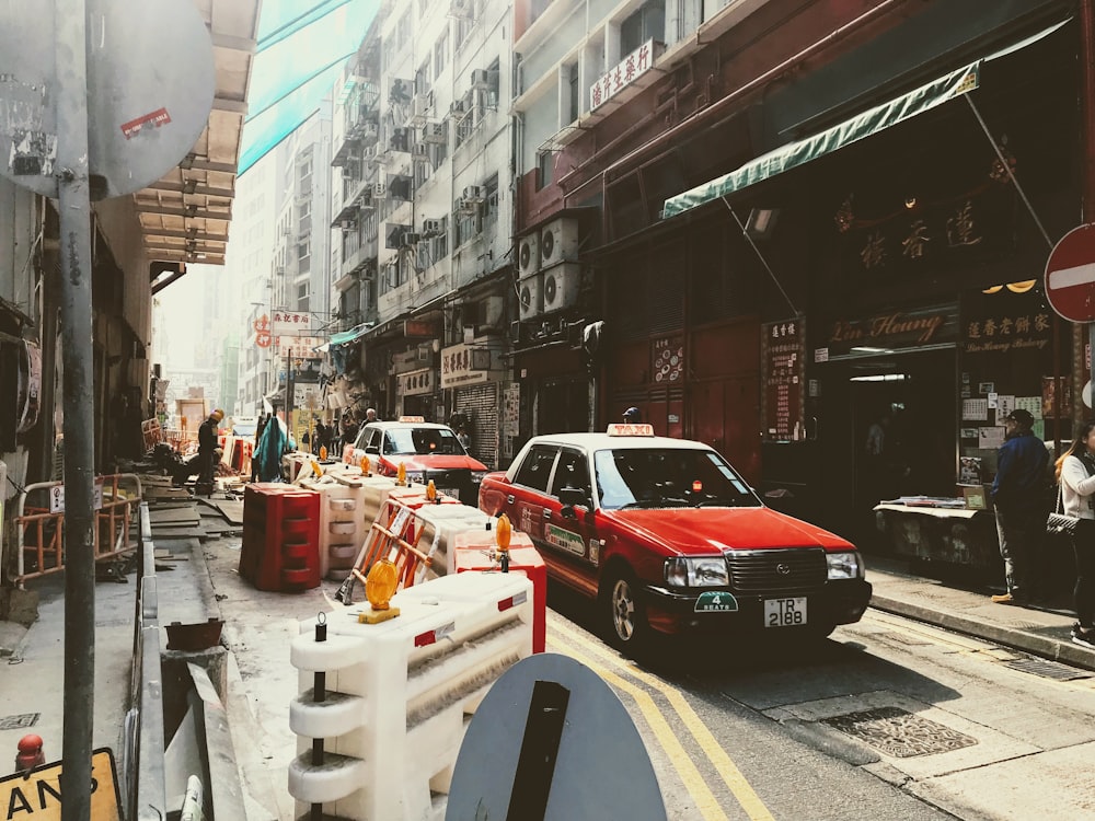 red sedan driving on concrete road between buildings