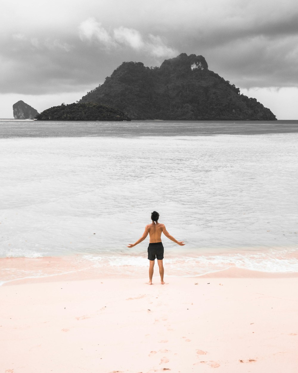 topless person standing near seashore raising both hands