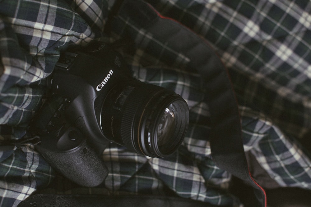 black Canon DSLR camera on black and white plaid textile