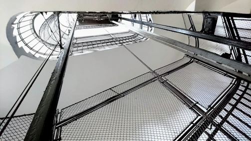 A sleek modern metal spiral staircase photographed from below with natural industrial lighting