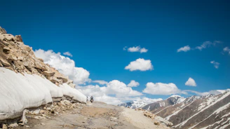 A rugged motorcycle winding along a high-altitude Himalayan mountain pass under clear blue skies.