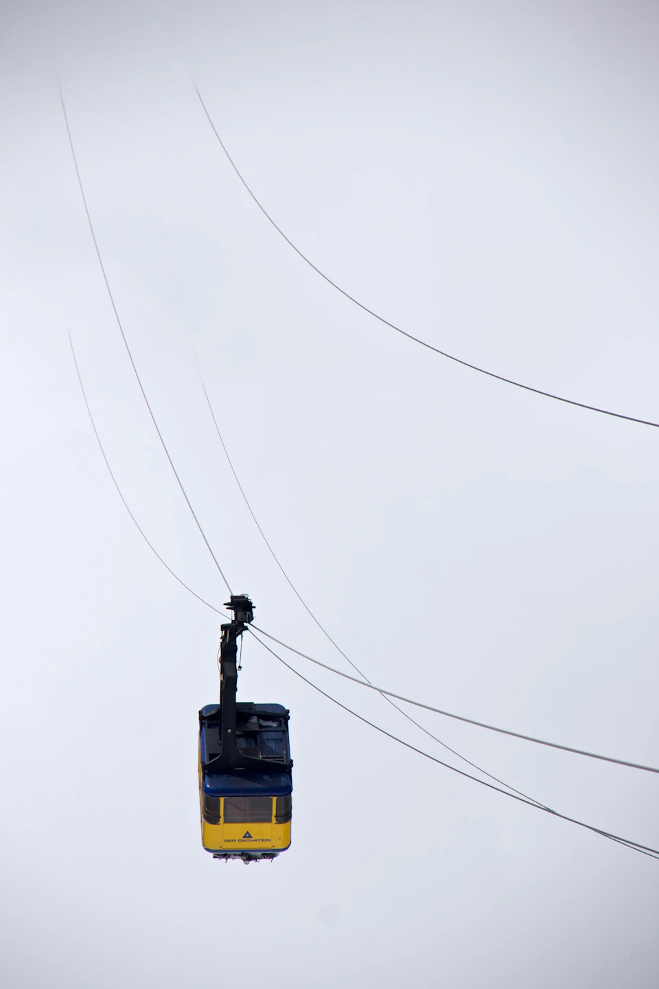 Cable car suspended mid-air with vibrant yellow and blue paint against light gray sky