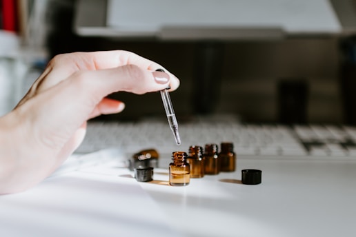 Close-up of a hand holding a pipette with glutadrops above a glass of water.