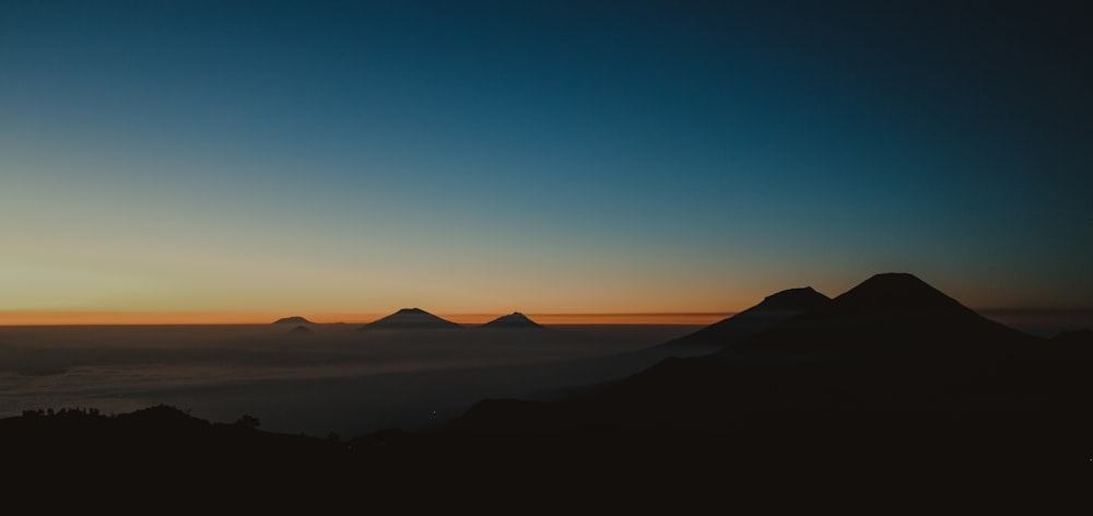 silhouette di montagne sotto il cielo blu e arancione durante l'ora d'oro