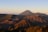 A stunning landscape of volcanic mountains at sunrise, with clear skies and gentle sunlight casting long shadows over the rugged terrain. Sparse vegetation covers some parts of the slopes, and a light mist or smoke rises from the caldera, adding an ethereal quality to the scene.