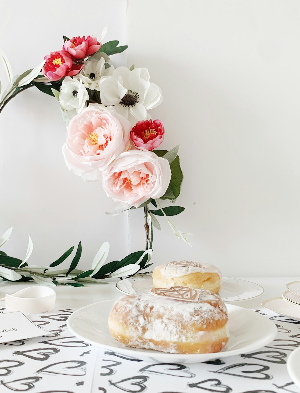 two doughtnuts on white ceramic plates beside petaled flowers