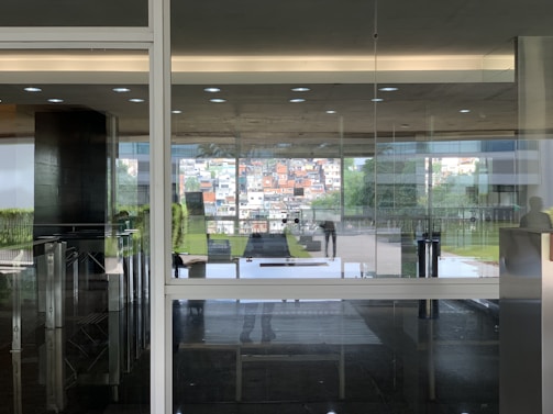 A modern glass office entrance with reflections of blue sky and greenery.