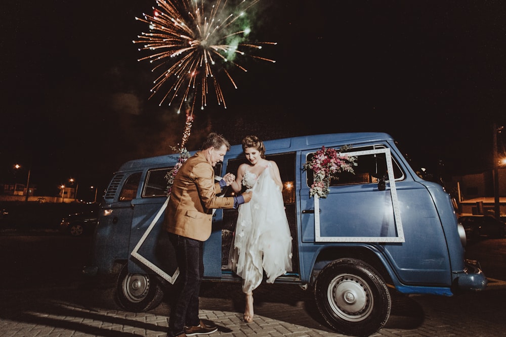 woman getting out of the blue van while holding a man during night time