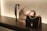 On a sleek black surface, a display features two elegantly designed handbags. The central bag is cream-colored with a scalloped edge and a silver chain handle, while the other is black with a gold chain. To the left, there's a decorative strap showcasing an intricate design.