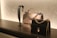 On a sleek black surface, a display features two elegantly designed handbags. The central bag is cream-colored with a scalloped edge and a silver chain handle, while the other is black with a gold chain. To the left, there's a decorative strap showcasing an intricate design.