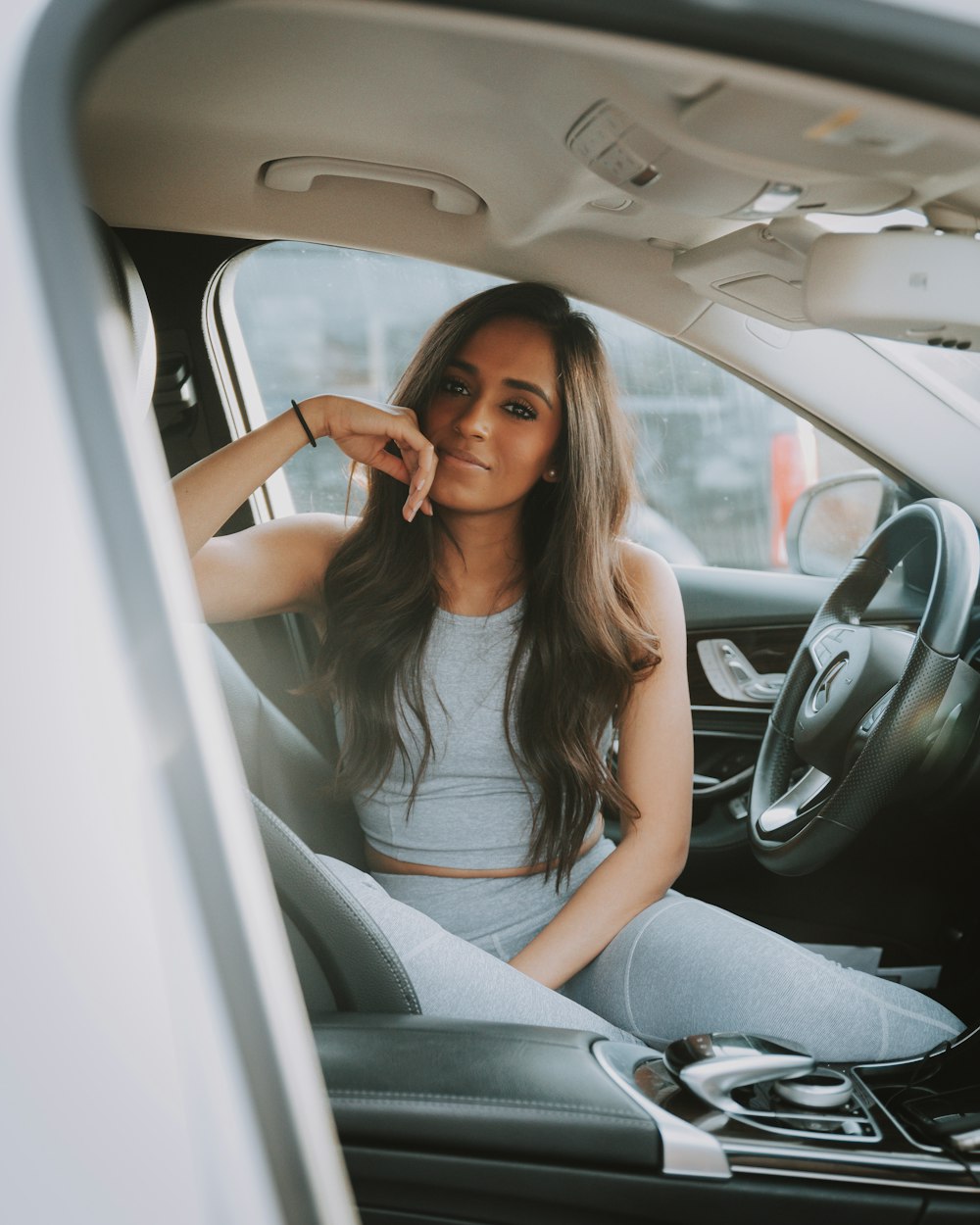 smiling woman sitting inside the car with hand on her chin