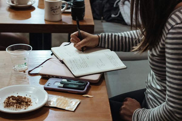 Woman writing a list in a notebook at a coffee shop table