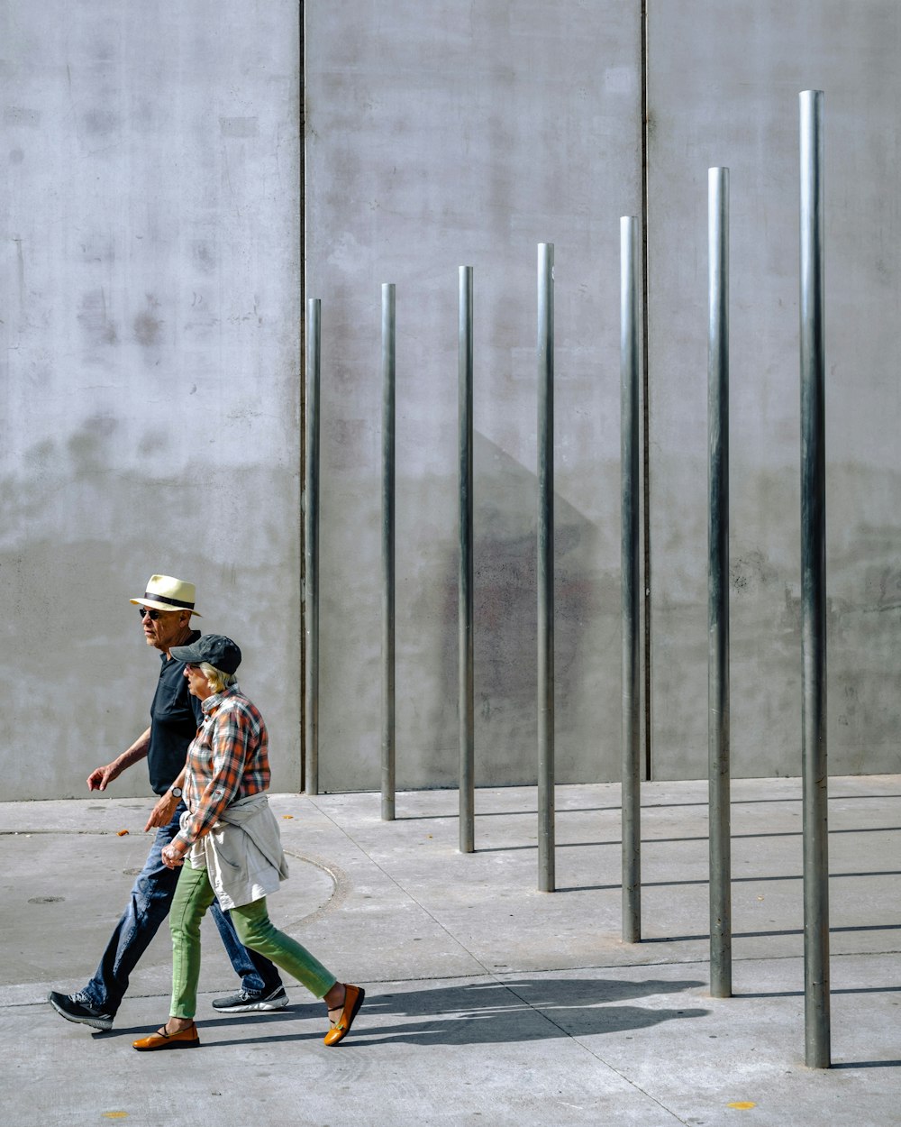 man and woman walking near stainless steel posts