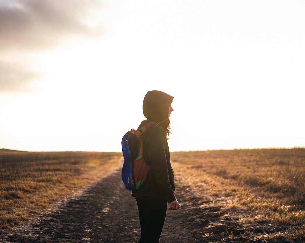 person wearing backpack standing on pathway during golden hour