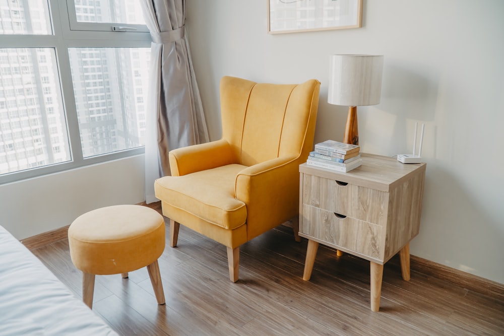 유리창과 침대 근처 벽 옆의 나무 협탁 옆에 있는 노란색 안락의자와 의자