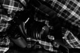 A DSLR camera with a Canon brand name is placed on a plaid fabric. The scene is captured in black and white, giving it a classic and timeless feel.