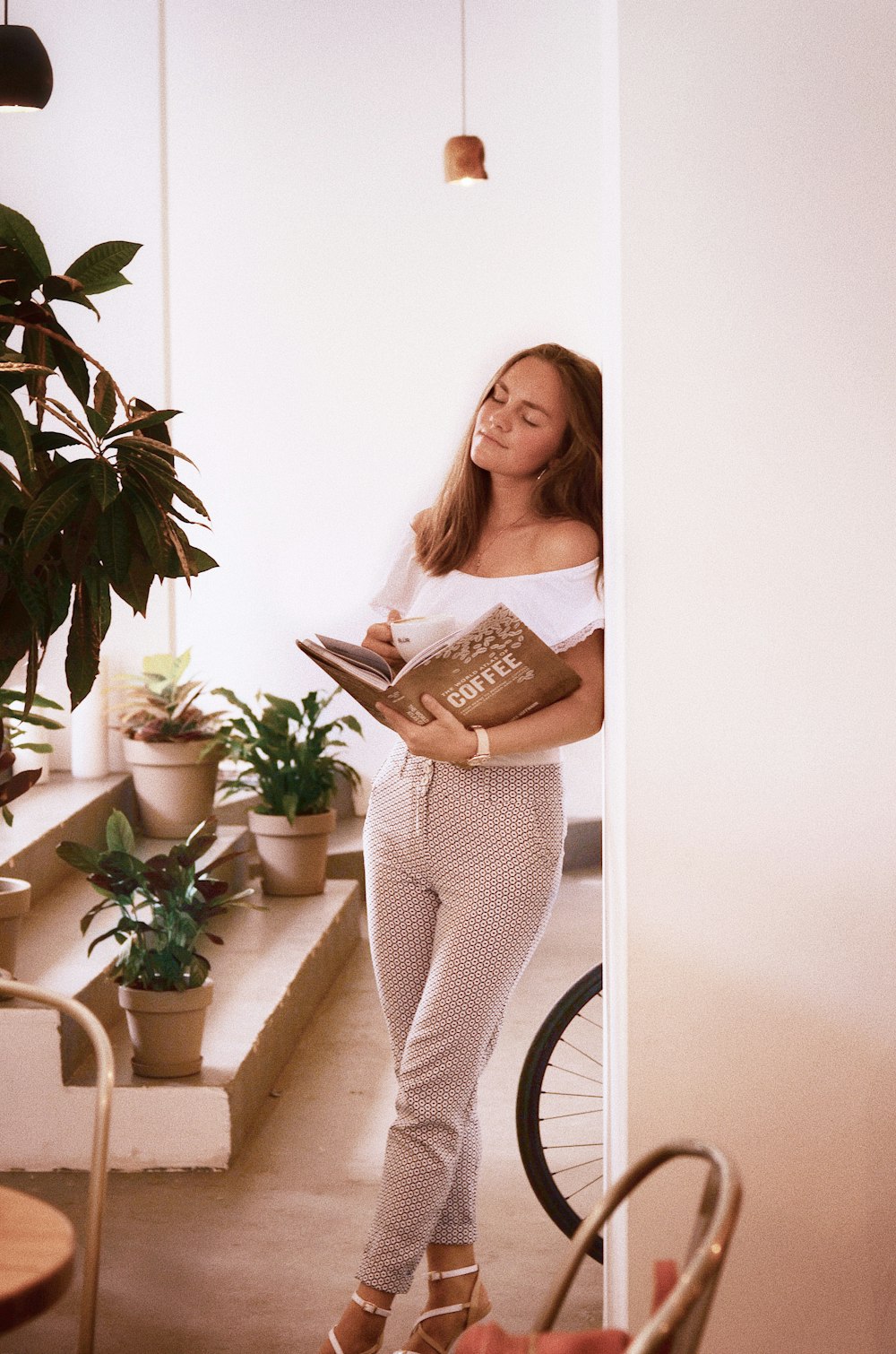 woman wearing white cap-sleeved shirt leaning on wall holding book