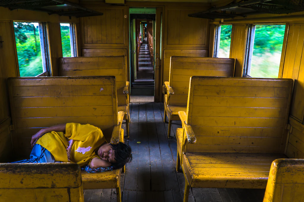 A passenger sleeping across yellow wooden seats inside an older Thai train carriage