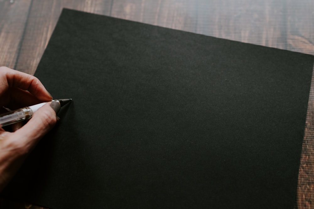 persona in procinto di scrivere su un foglio nero vuoto