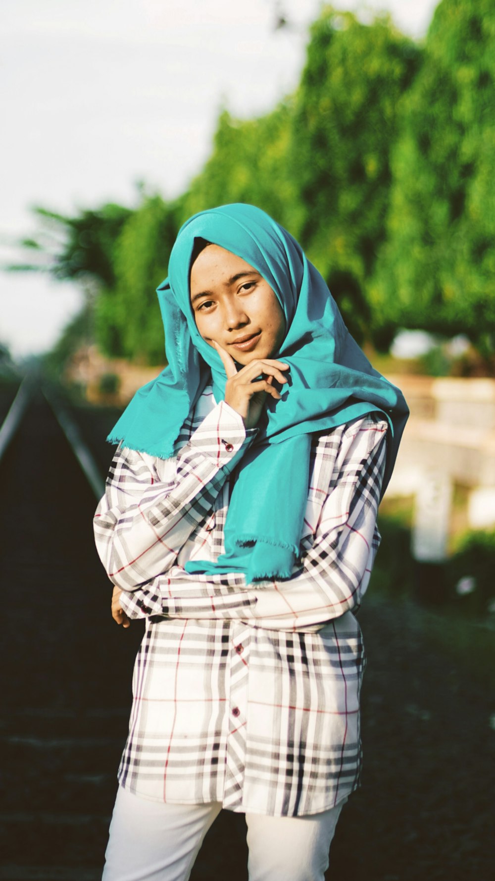 woman in blue hijab headscarf standing near green tree in selective focus photography
