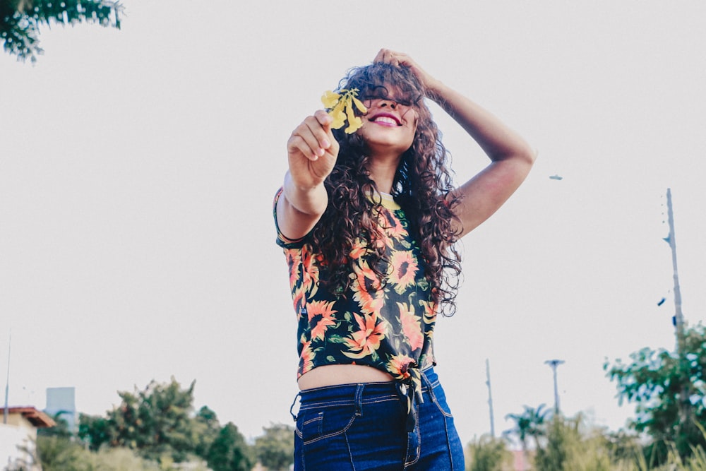 woman in floral sleeveless blouse holding yellow flower during daytime