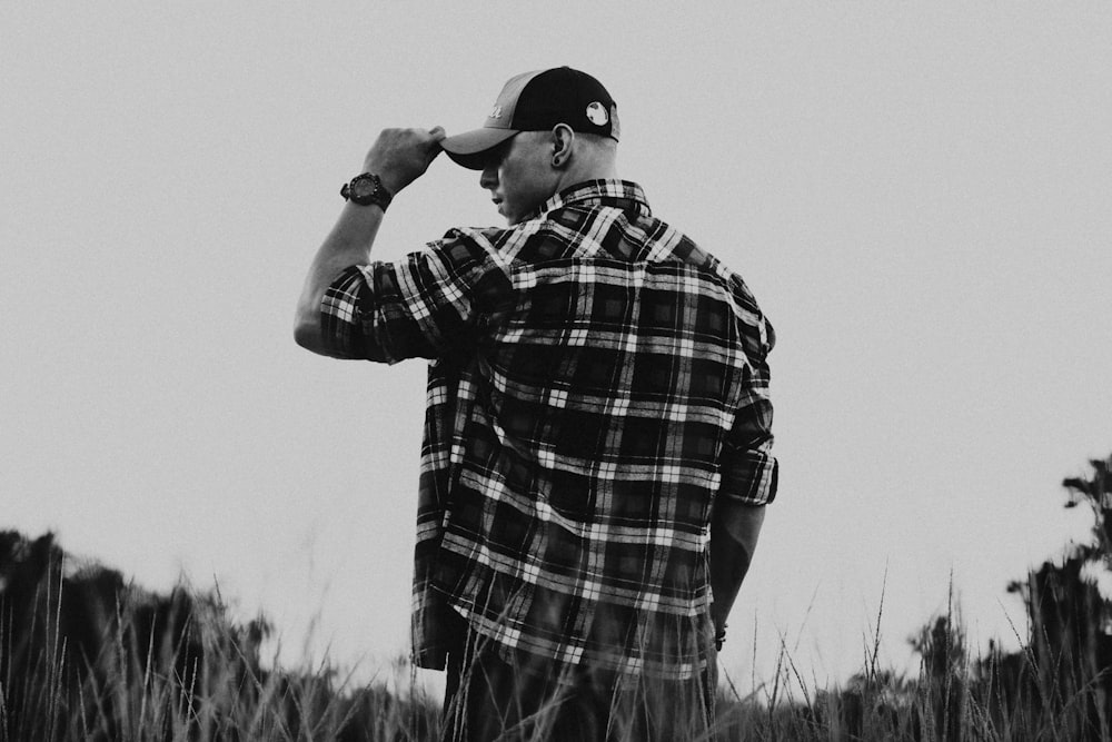 man holds cap while standing beside grass