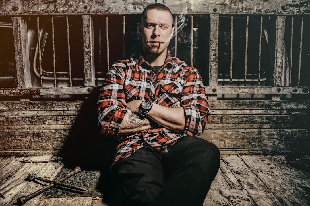 man smoking a cigarette while leaning and sitting on metal rail