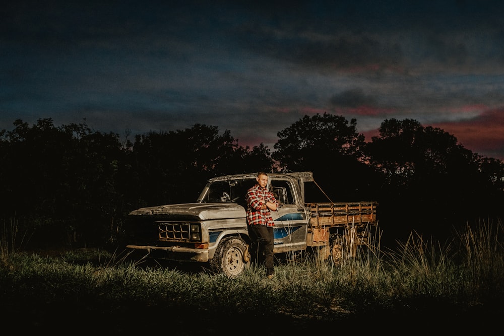 man leaning on his grey truck at the grass field