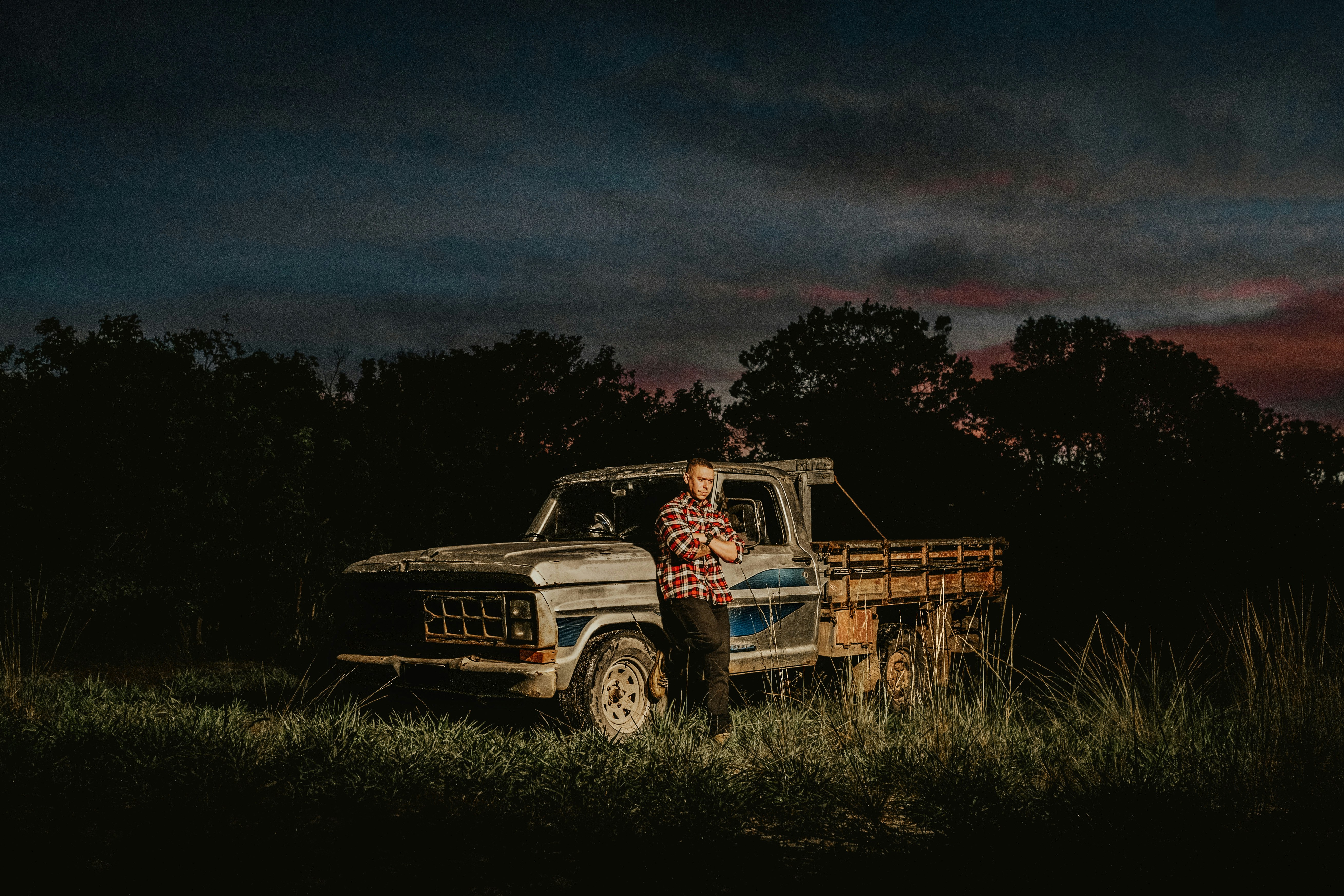 man leaning on his grey truck at the grass field